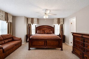 A bedroom with a wooden bed, a leather sofa, a dresser, and a ceiling fan. - Luxury Getaway 4 Bd/5 Bath 25 Mins to DisneyMagic! (Davenport)