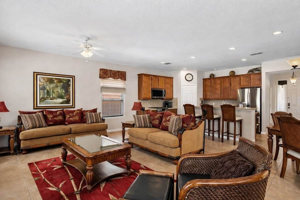 A spacious living room with a sofa, chairs, and a coffee table. There is a kitchen area with cabinets and appliances in the background.