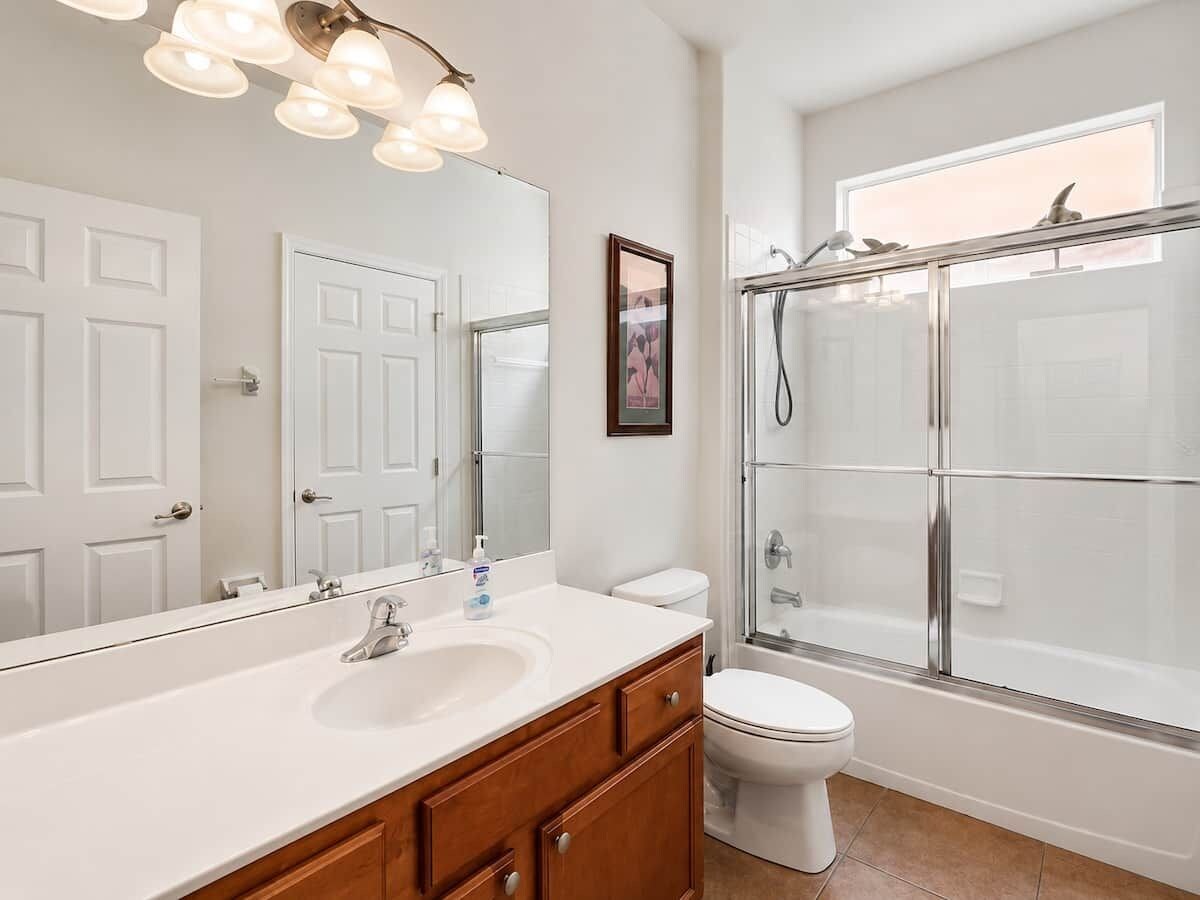 Un baño con lavamanos blanco, mueble de madera, inodoro blanco y cabina de ducha con paredes de vidrio.