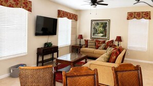 A living room with a sofa, chairs, a coffee table, a television, and a ceiling fan. - Luxury Getaway 4 Bd/5 Bath 25 Mins to DisneyMagic! (Davenport)