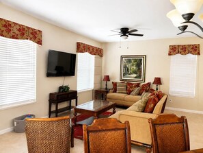 A living room with a sofa, chairs, a coffee table, a television, and a ceiling fan. - Luxury Getaway 4 Bd/5 Bath 25 Mins to DisneyMagic! (Davenport)