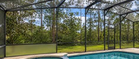A swimming pool with a hot tub, surrounded by a covered area with a view of trees.