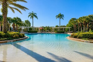 A clear swimming pool with a 6-inch depth marker, surrounded by palm trees and a pergola structure. - Luxury Getaway 4 Bd/5 Bath 25 Mins to DisneyMagic! (Davenport)