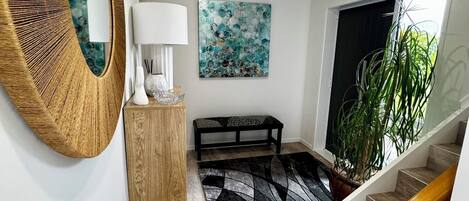 Un interior moderno con suelo de madera, un espejo redondo, un banco, un cuadro y una escalera.