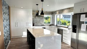 A modern kitchen with a central island, stainless steel appliances, and a view of greenery outside. - Views @ Four Winds (Taupō)