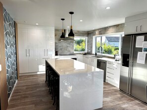 A modern kitchen with a central island, stainless steel appliances, and a view of greenery outside. - Views @ Four Winds (Taupō)