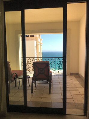 Un balcón con vista al océano, una silla y una mesa.