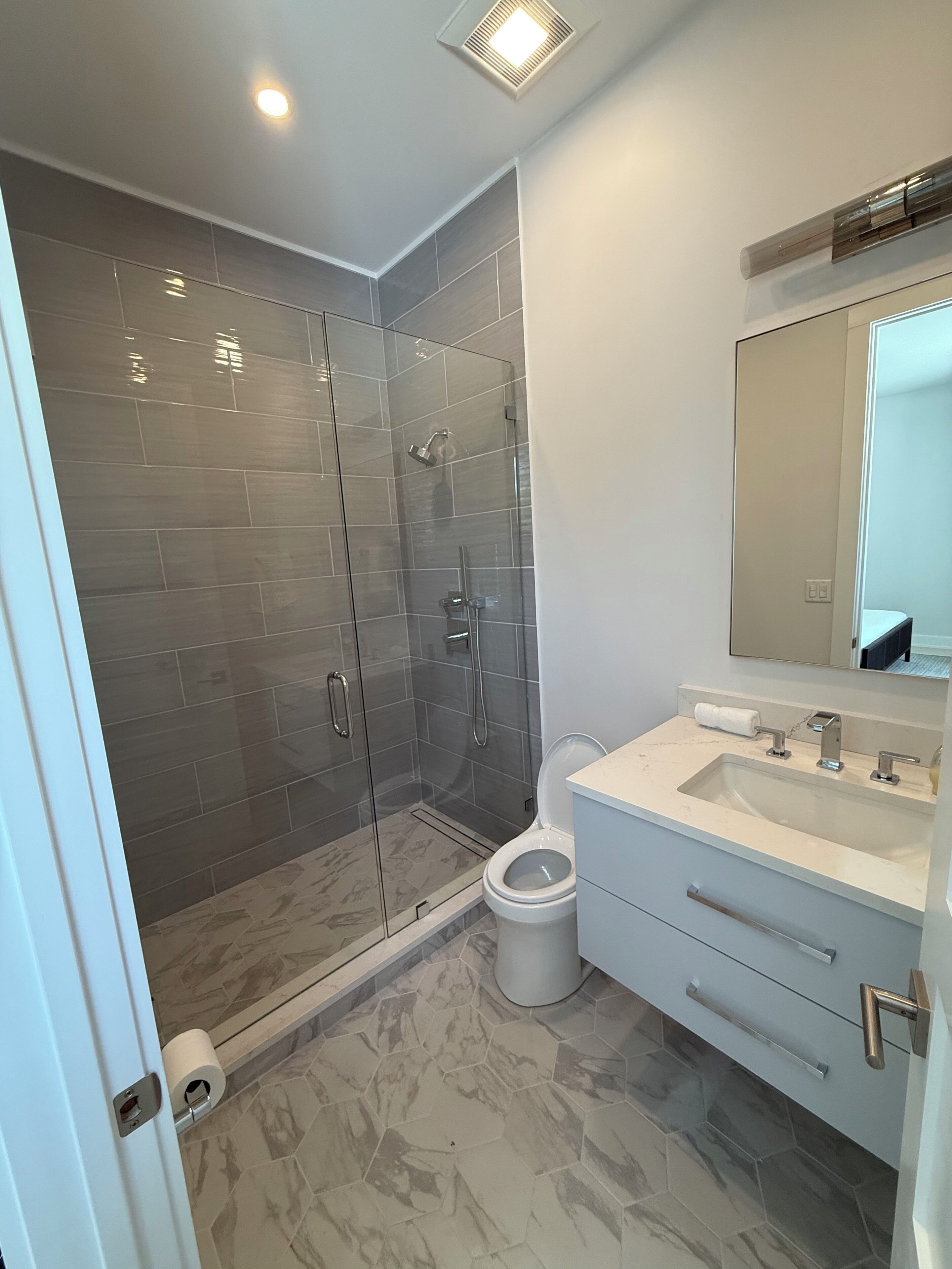Une salle de bain moderne avec une douche à parois de verre, des toilettes blanches et un meuble-lavabo avec un évier et un miroir.