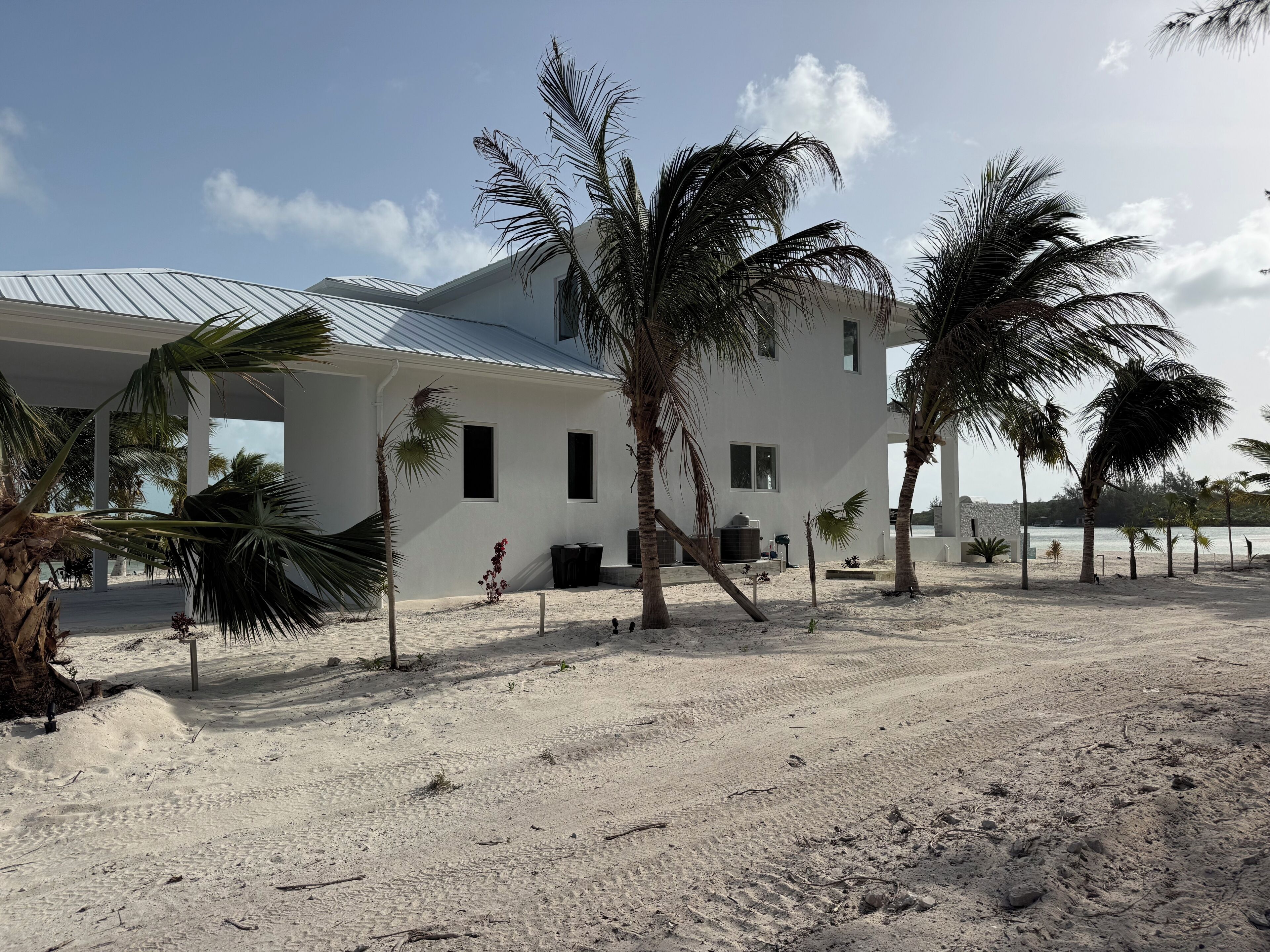 Un bâtiment blanc surmonté d’un toit en métal, entouré de palmiers et bordé d’une plage de sable.