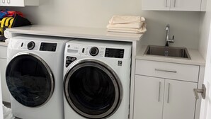 A laundry area with two front-loading washing machines, a sink, and a cabinet with a towel rack. - Enchanting Luxury Beachfront Villa Stillwater in Sandy Point views of Parrot Cay (Sandy Point)