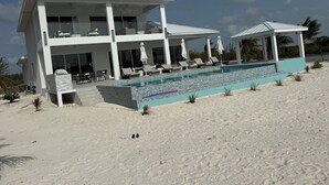 A two-story beachfront property with a swimming pool, lounge chairs, and umbrellas. - Enchanting Luxury Beachfront Villa Stillwater in Sandy Point views of Parrot Cay (Sandy Point)