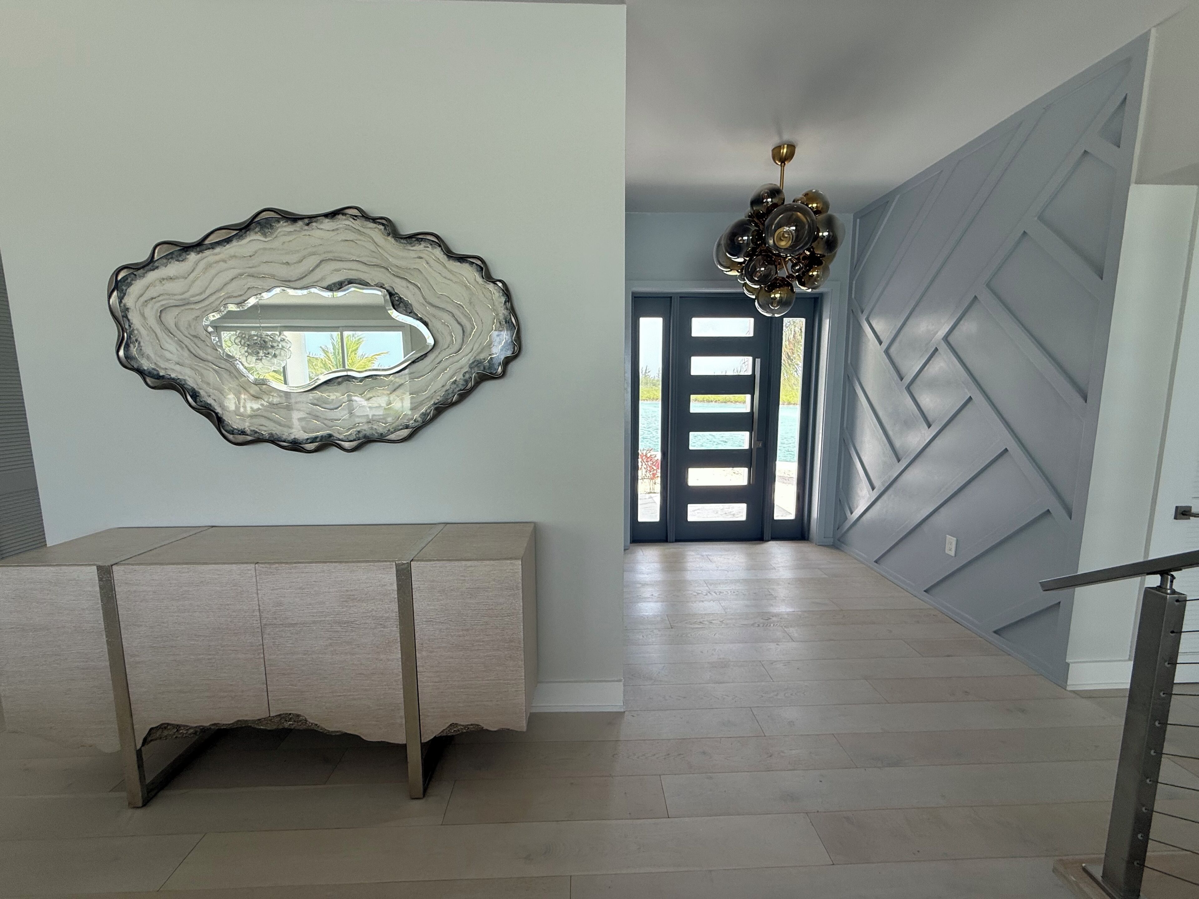 Un couloir doté d’un plancher en bois de couleur claire, d’un élément décoratif mural et d’une vue sur un espace extérieur, visible à travers une porte.