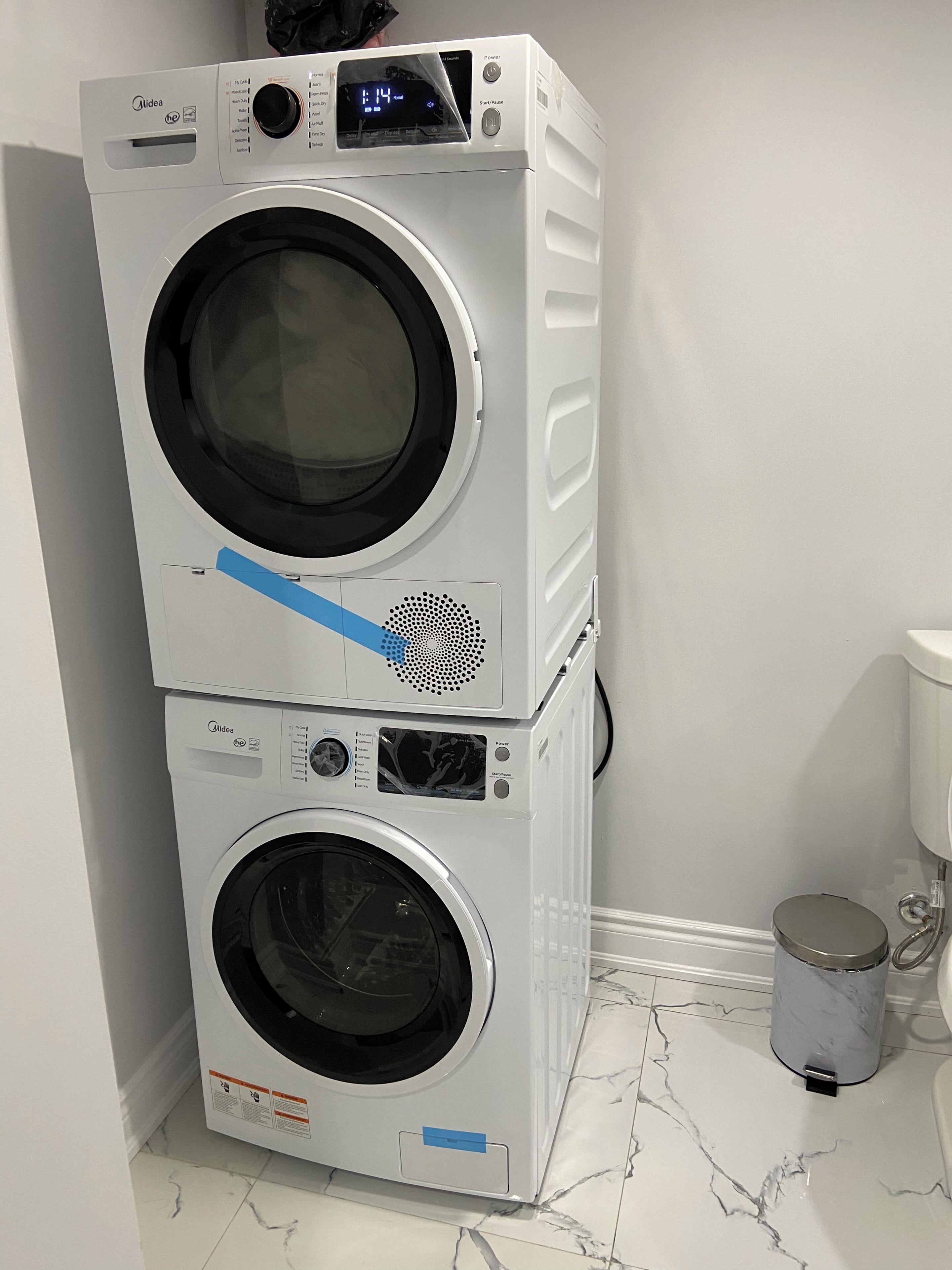 Een wasmachine en droger boven elkaar in een badkamer met een marmeren vloer.