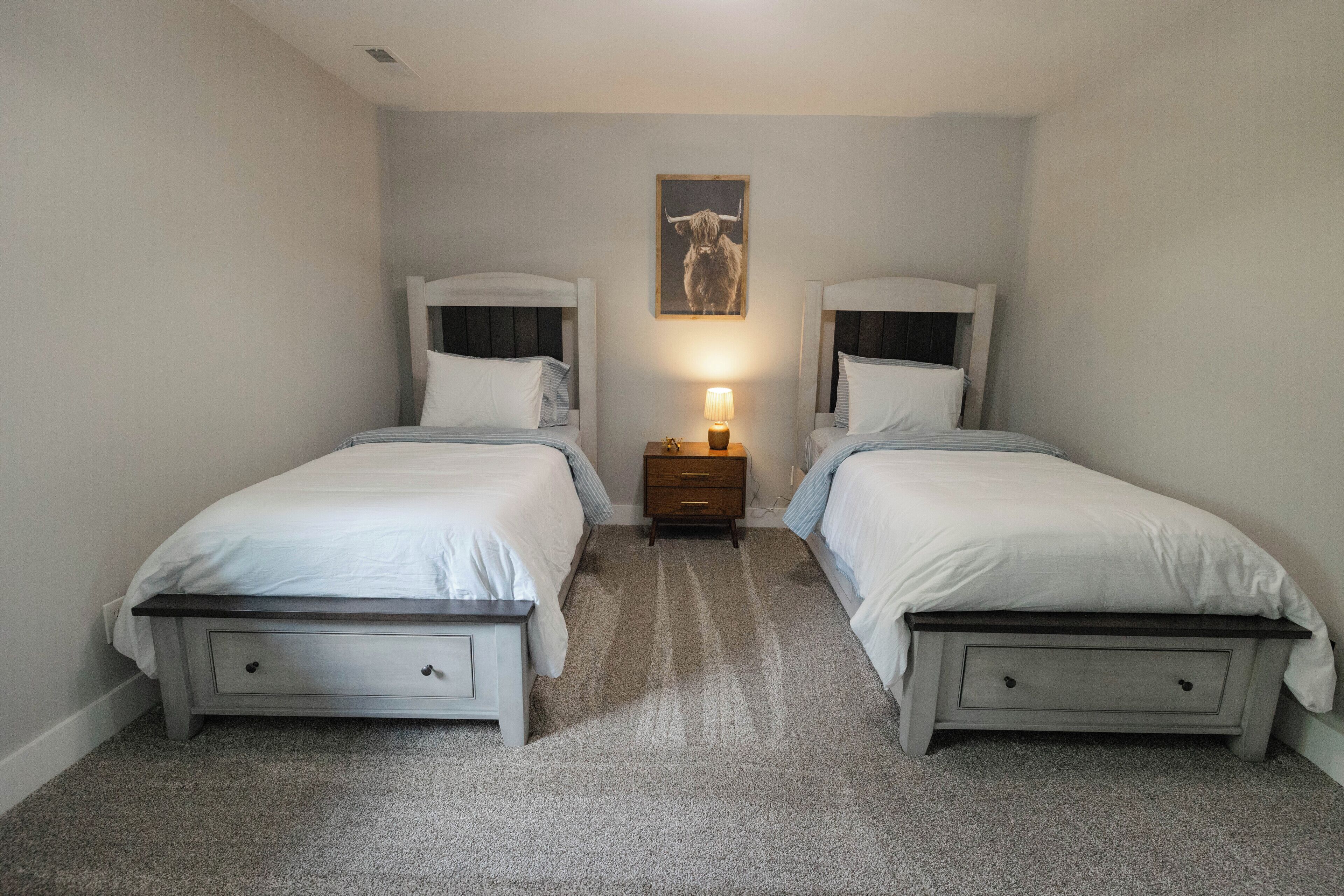 A bedroom with two beds, a nightstand with a lamp, and a framed picture on the wall.