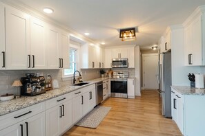 A modern kitchen with white cabinetry, stainless steel appliances, and a marble countertop.