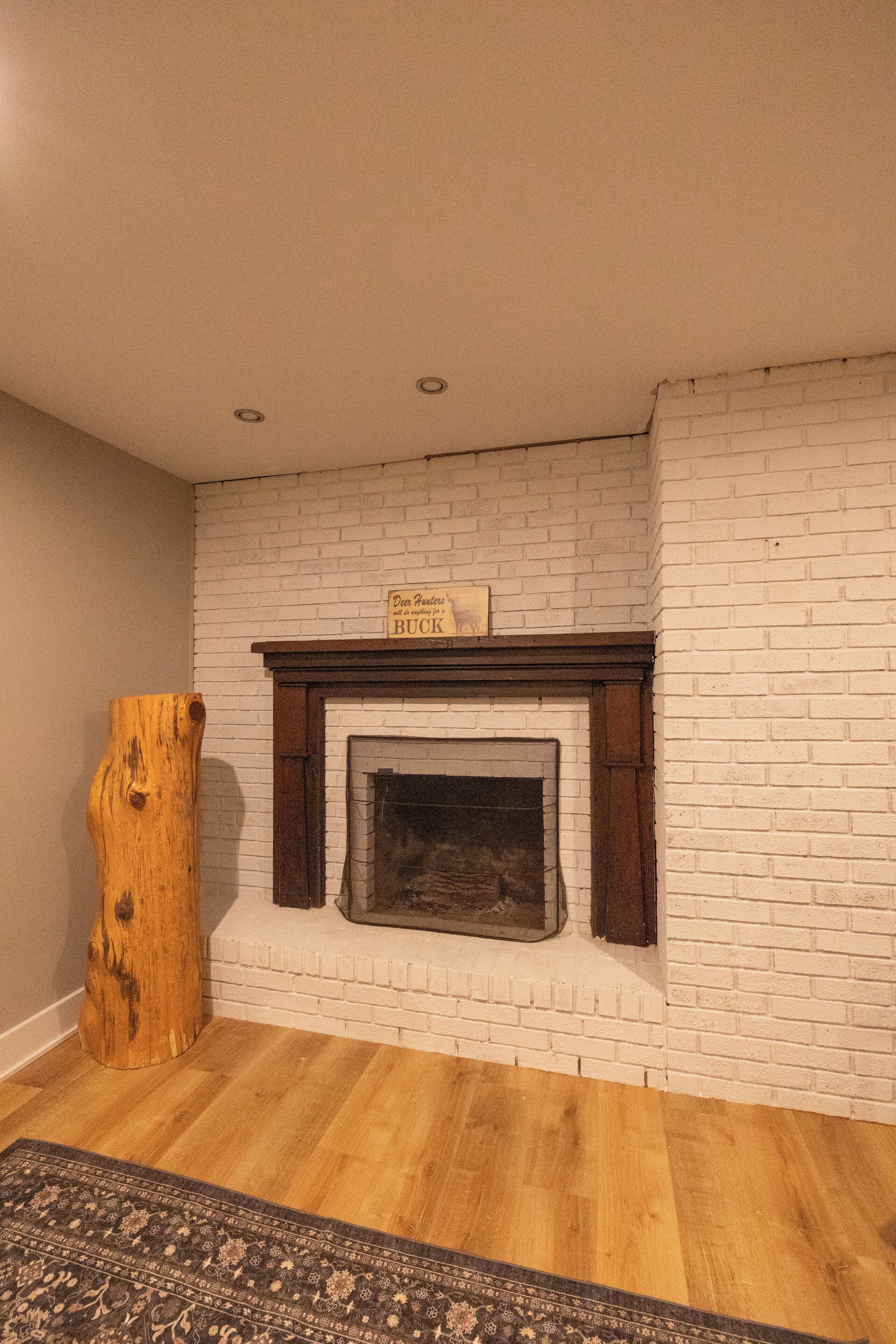 A room with a white brick fireplace, a wooden log, and a patterned rug.