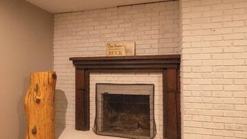 A room with a white brick fireplace, a wooden log, and a patterned rug.