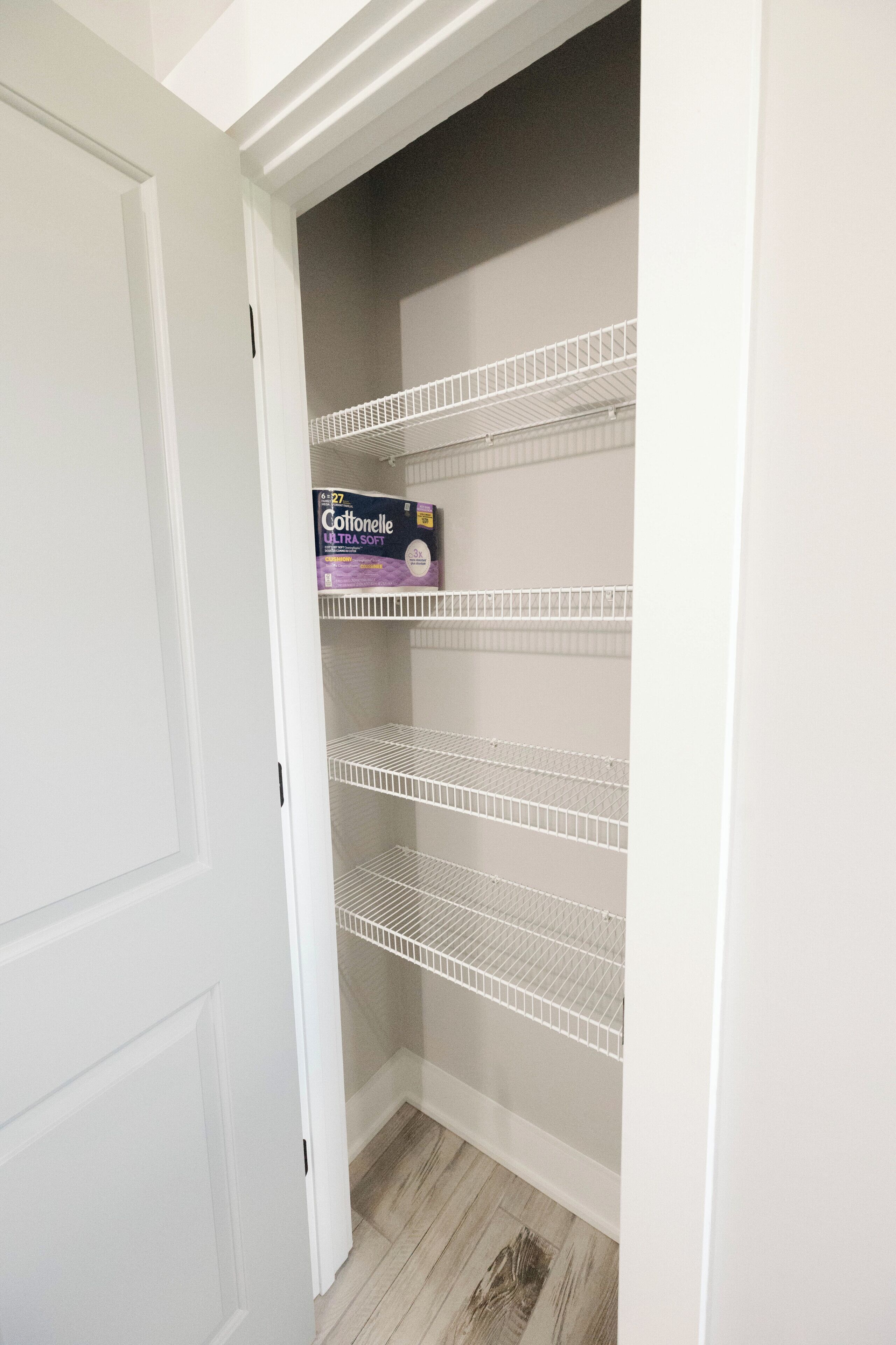 A white closet with three wire shelves and a box of Cottonelle Ultra Soft toilet paper.