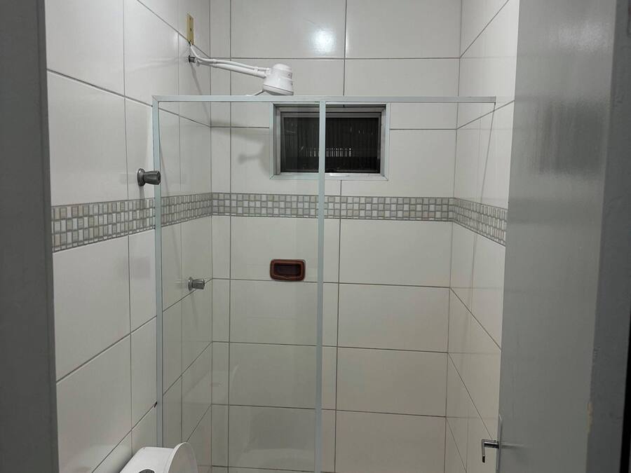 Un baño con cabina de ducha de vidrio, inodoro y una ventana pequeña.