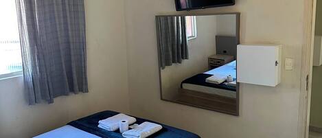 A hotel room with a bed, a television, a mirror, and a window with curtains.