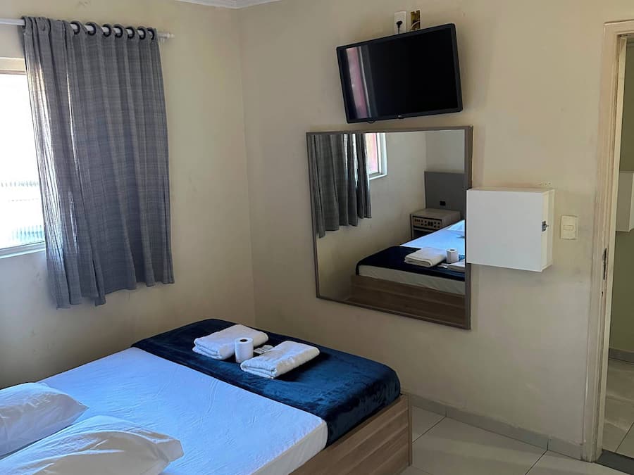 Una habitación de hotel con cama, televisión, espejo y ventana con cortinas.