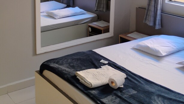Ein Schlafzimmer mit einem Bett, einem Nachttisch, einem Spiegel und einem Fenster mit Vorhängen.