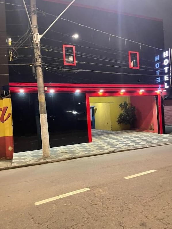 A hotel entrance with a red and black facade, a tiled entrance area, and a visible signboard.
