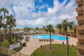 A pool area with lounge chairs, palm trees, and a sign indicating pool rules. - Sandpiper 1005: Oceanfront 3BR condo with pool, hot tub, and beach access in Port Aransas. (Port Aransas)