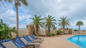 A poolside area with lounge chairs, palm trees, and a pool. - Sandpiper 1005: Oceanfront 3BR condo with pool, hot tub, and beach access in Port Aransas. (Port Aransas)