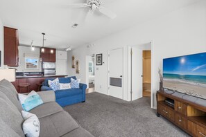Ein modernes Wohnzimmer mit einem blauen Sofa, einem grauen Couch und einer Küchenzeile, mit Blick auf den Strand durch ein großes Fenster.