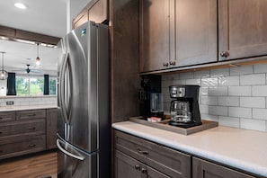 A kitchen with wooden cabinets, a stainless steel refrigerator, a coffee maker, and a window with curtains. - Casa de Cozy - Resort Condo Minutes from Branson & Lake Taneycomo (Branson)