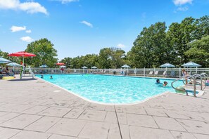 Ein Schwimmbecken mit Fliesen, Sonnenschirmen und einem weißen Zaun.