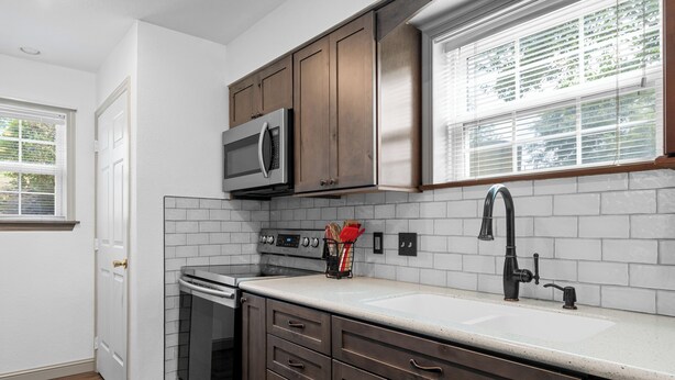 A kitchen with white subway tiles, dark wooden cabinets, a stainless steel microwave, and a built-in oven. - Casa de Cozy - Resort Condo Minutes from Branson & Lake Taneycomo (Branson)