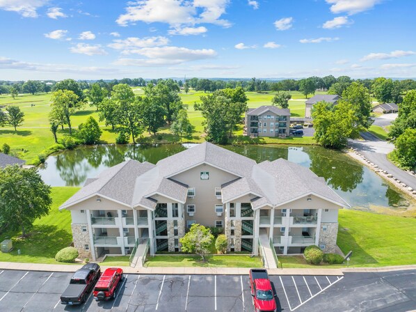 A multi-story building with a central courtyard, parking lot, and a pond. - Casa de Cozy - Resort Condo Minutes from Branson & Lake Taneycomo (Branson)