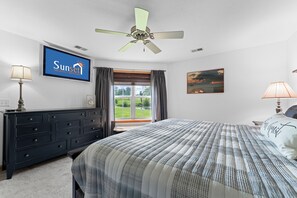 A bedroom with a bed, a dresser, a ceiling fan, a TV displaying a logo, a window with curtains, and a painting on the wall. - Casa de Cozy - Resort Condo Minutes from Branson & Lake Taneycomo (Branson)