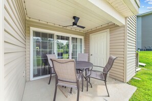 Eine überdachte Terrasse mit Tisch und Stühlen, einer Schiebetür aus Glas und einem Deckenventilator.