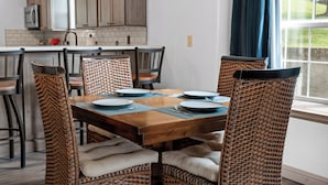 A dining area with a wooden table, wicker chairs, and a view of the kitchen in the background. - Casa de Cozy - Resort Condo Minutes from Branson & Lake Taneycomo (Branson)