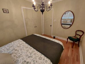 A bedroom with a bed, a chair, a mirror, and a chandelier.