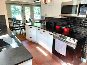 A kitchen with white cabinets, a black countertop, a stainless steel stove, and a microwave. - Central 3BR Oasis: Private 5 Person Sauna , Spa Bath & Yard [Sleeps 7, 4 Beds] (Greater Sudbury)