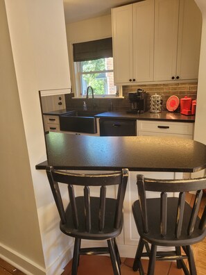 A kitchen with a black countertop, white cabinets, a window, and a coffee maker.