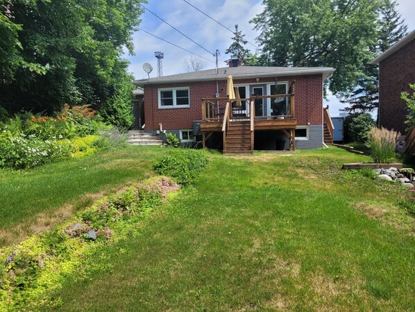 A two-story brick house with a wooden deck and a small staircase leading to the front door.