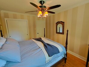 A bedroom with a bed, a ceiling fan, a mirror, and striped wallpaper.