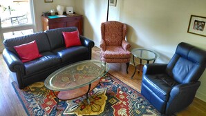 Una sala de estar con un sofá de cuero, un sillón estampado, una mesa de centro de vidrio y un sillón azul.