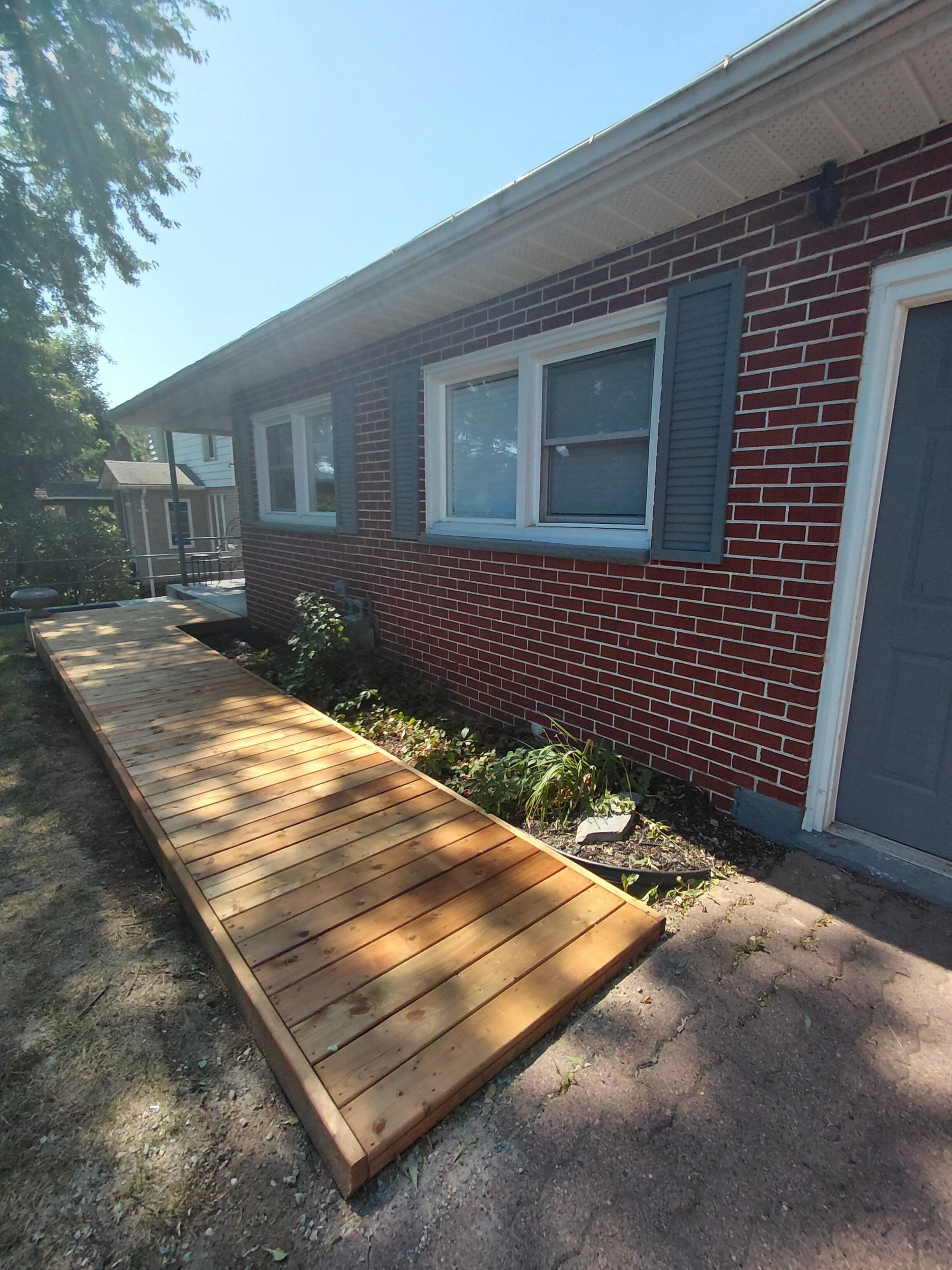 Un immeuble résidentiel avec une façade en briques, une terrasse en bois et un petit jardin.