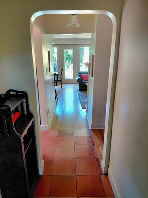 Corredor que dá para uma sala de estar, com uma porta, uma cadeira e um sofá.