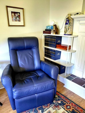 A blue leather armchair, a bookshelf with books and decorative items, and a framed picture on the wall.