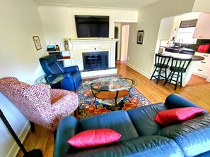 A living room with a fireplace, a sofa, a coffee table, and a kitchen area with bar stools.