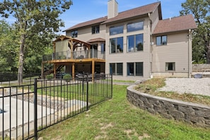 A two-story house with a balcony, a stone retaining wall, and a fenced backyard. - Heated Pool, Game Room & Outdoor Living Near Ha Ha Tonka (Camdenton)
