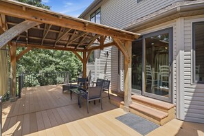 A wooden deck with outdoor furniture, a covered area, and a house with large windows.