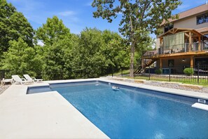 A swimming pool with lounge chairs, a covered deck, and a house with a balcony. - Heated Pool, Game Room & Outdoor Living Near Ha Ha Tonka (Camdenton)
